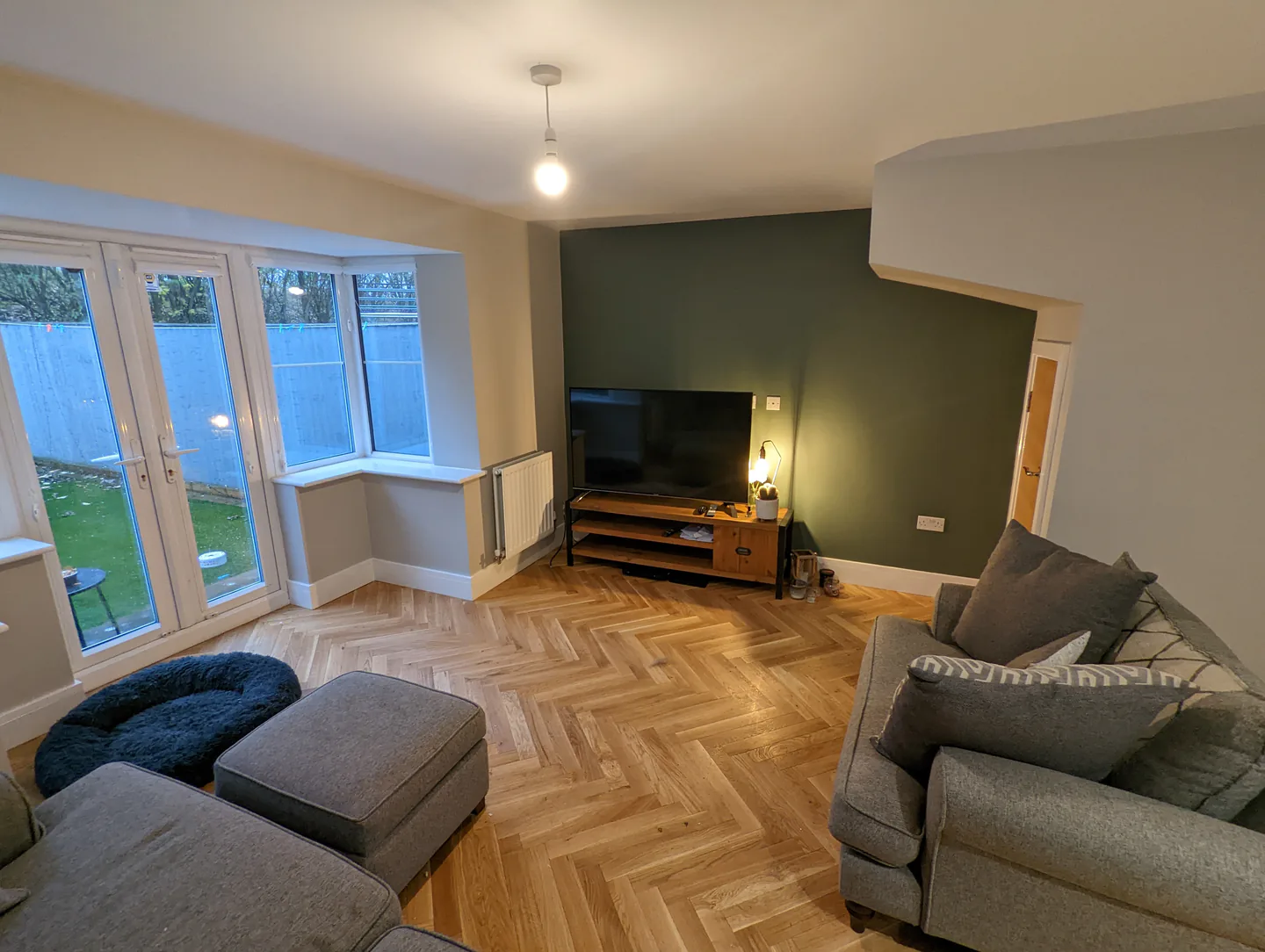 Finished lounge with a deep green feature wall and herringbone wood floor